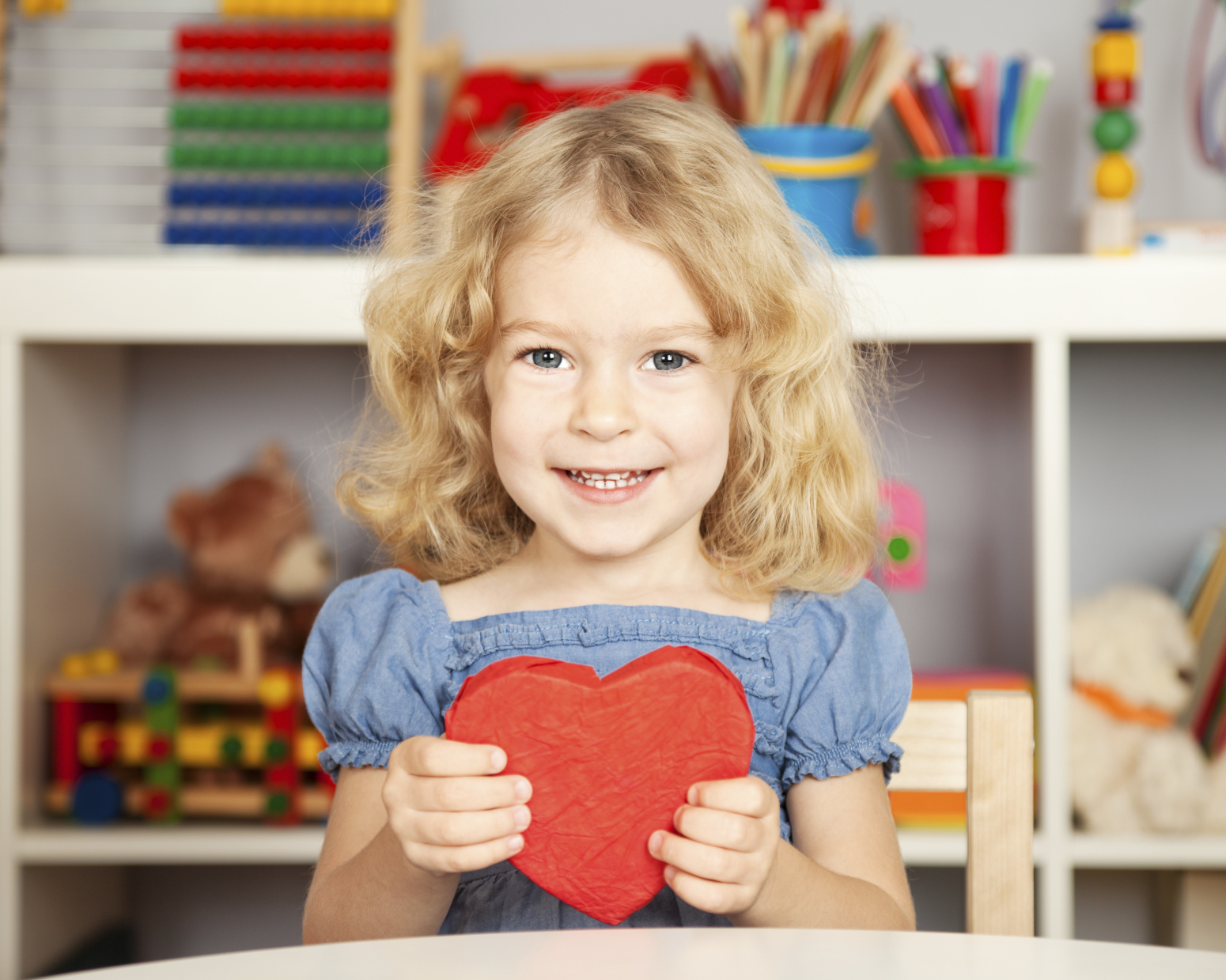 Happy child with handmade paper red heart in class. School concept